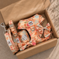 Floral dog harness and leash set in a cardboard box on a stone surface.