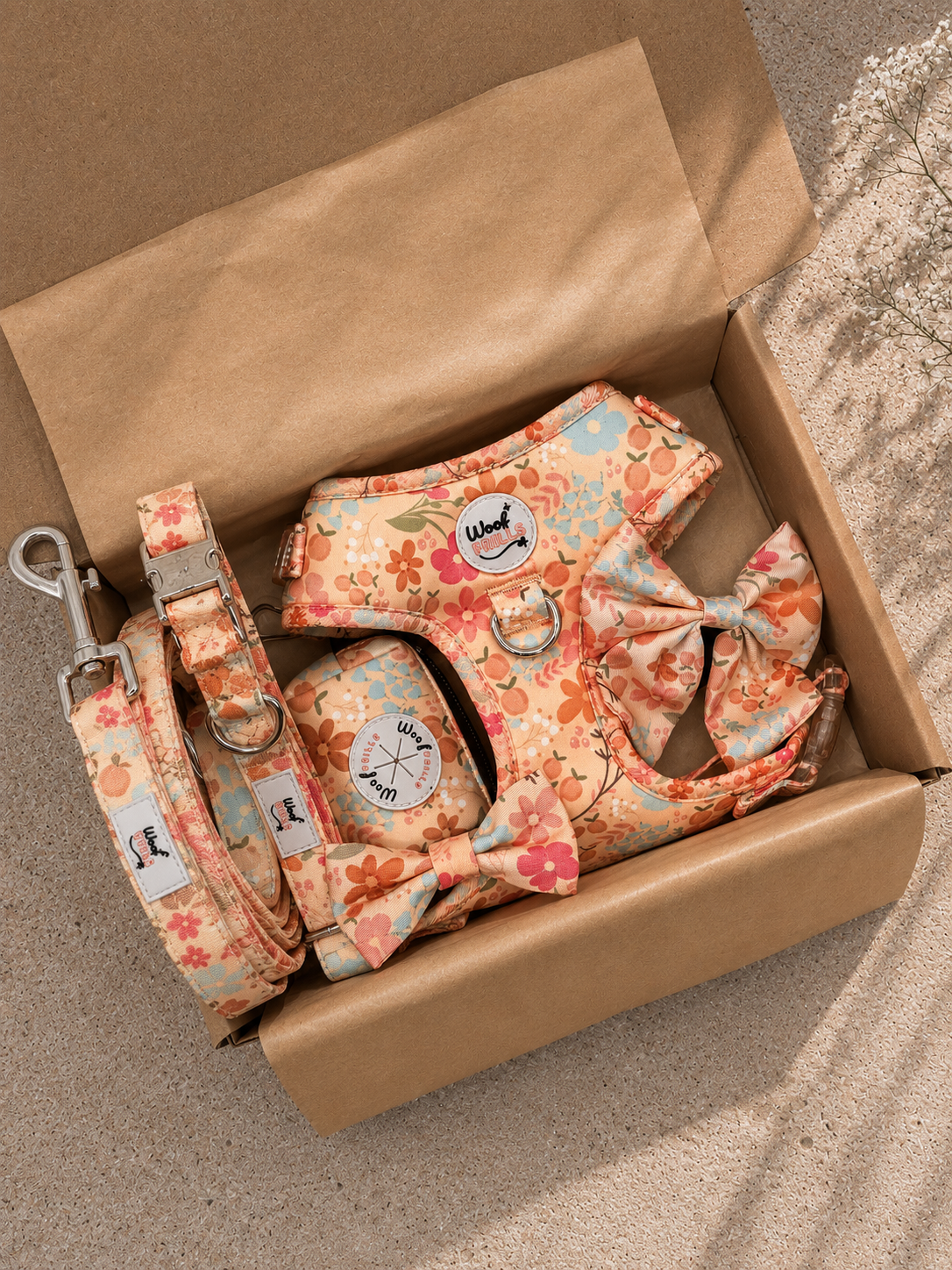 Floral dog harness and leash set in a cardboard box on a stone surface.