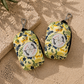 Two floral-patterned poo bag holders on a sandy surface with palm leaves.