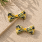 Two yellow floral dog bow ties on a textured beige surface with leaves in the corner.