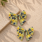 Two floral-patterned dog sailor bows on a textured beige surface with a leafy branch.