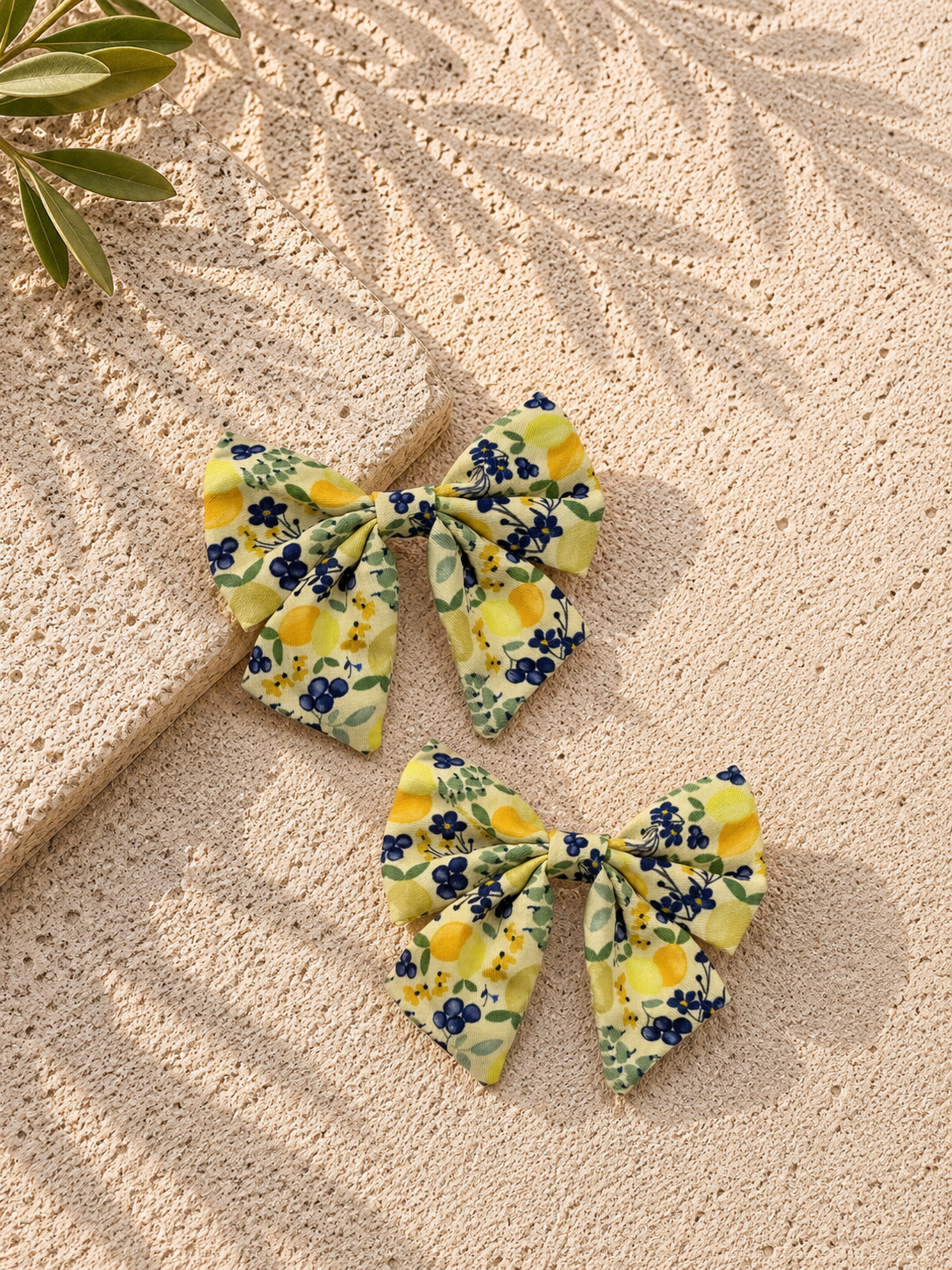 Two floral-patterned dog sailor bows on a textured beige surface with a leafy branch.