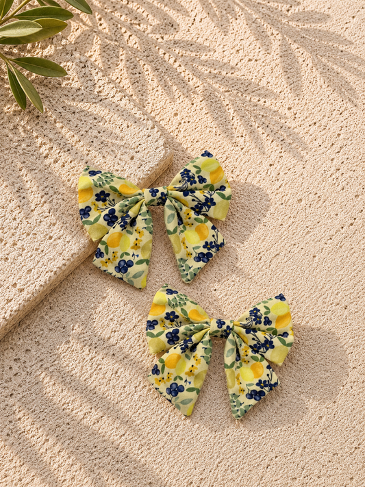 Two floral-patterned dog sailor bows on a textured beige surface with a leafy branch.